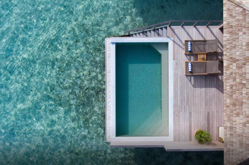 This captures the secret of a great tourism photo. A floating pool sitting on the edge of the ocean, with an attached deck that shows two lounge charis.