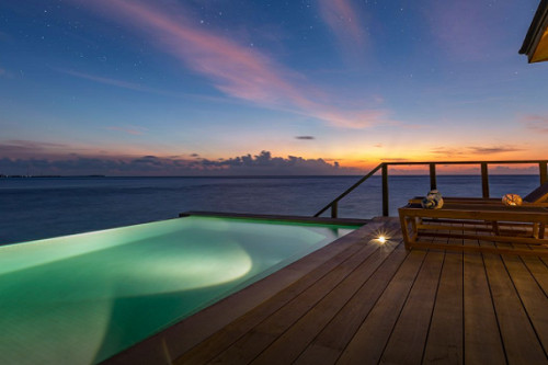 From the perspective standing on a deck looking out at the edge of a floating pool and the Indian Ocean just after sunset.