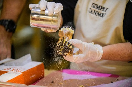 A person shaking powdered sugar onto a cannoli that's covered with chocolate chips.